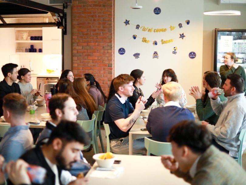Zeta Global team members chat while eating lunch together at various tables in the office on Employee Appreciation Day 2025